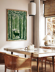 Green linocut style art print of a stag with antlers standing in a dense forest of tall trees, in a styled room mockup