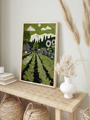 Green garden linocut-style print with vegetable rows, barns, sunflowers, mountains, and sun, in an alternate framed mockup
