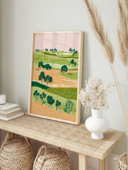 Illustrative green landscape art print with rolling hills, orange fields, and dark green, in an alternate framed mockup