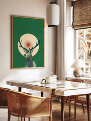 Illustrative green stag with antlers, set against a cream circle and red sunburst on a dark green, in a styled room mockup