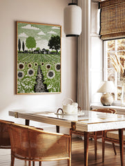 Green linocut print of a sunflower field with a path leading to a farm and trees under a cloudy sky, in a styled room mockup