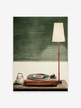 Green vinyl record player poster with wooden turntable, floral teapot and floor lamp against textured green wall