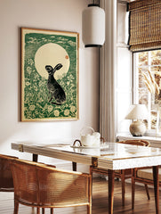 Woodcut print of a black hare looking up at a large white moon, surrounded by green grass and, in a styled room mockup