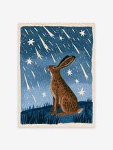 Brown hare sitting in a grassy meadow looking up at a meteor shower in a blue night sky, illustrative wall art print