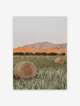 Photographic print of a field with hay bales, green grass, a row of trees, orange hills, and mountains under a grey sky.