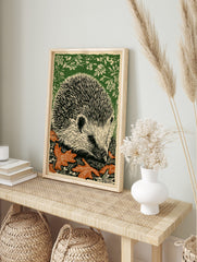 Woodcut style art print of a hedgehog amongst green foliage and orange autumn leaves, facing, in an alternate framed mockup