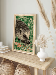 Woodcut illustration art print of a hedgehog in green foliage with some orange autumn leaves, in an alternate framed mockup