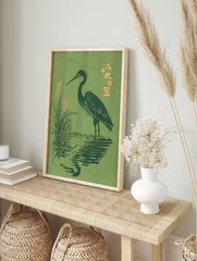 Japanese woodblock-style print of a dark green heron wading in water with golden reeds and, in an alternate framed mockup