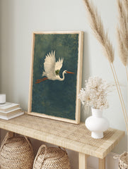 Illustrative print of a white heron flying horizontally with a green frog on its back against, in an alternate framed mockup