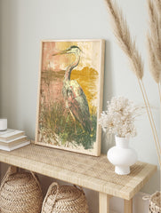 Illustrative art print of a heron bird standing in tall grasses by water, with a muted pink, in an alternate framed mockup