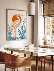 Illustrative heron bird print with orange outline, orange sun, and blue reeds on white background, in a styled room mockup