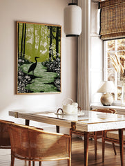 Linocut-style print of a black heron standing in a green forest stream with white flowers and tall, in a styled room mockup