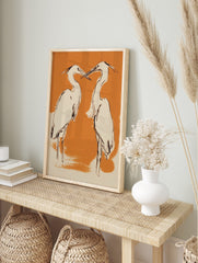 Illustrative art print of two herons with black outlines, cream bodies, on an orange, in an alternate framed mockup