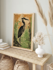 Illustrative heron bird art print in black, green, and orange, standing in a marsh with reeds, in an alternate framed mockup