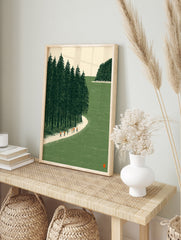 Illustrative wall art of hikers on a sandy path next to a green pine forest and water, in an alternate framed mockup