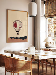 Illustrative red and cream hot air balloon floating above abstract brown and dark grey hills on a, in a styled room mockup