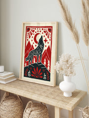 Howling wolf against red moon and stars, framed by mountains and folk art border in red, in an alternate framed mockup