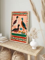 Illustrative print of three ducks, coffee cup, and croissants on a pink background with a red, in an alternate framed mockup