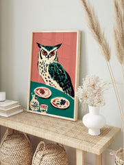 Illustrative owl with orange eyes on teal table with plates and pottery, pink background, in an alternate framed mockup