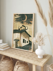 Japanese-style illustration of two cats sitting on a tiled roof beneath a crescent moon, in an alternate framed mockup