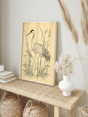 Japanese crane bird illustration standing in reeds, black ink on beige, with red signature, in an alternate framed mockup
