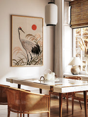 Japanese red-crowned crane illustration with tall reeds and a red sun, textured embroidery-style, in a styled room mockup