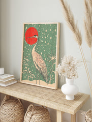 Japanese crane standing in snow with red sun and snowflakes in woodblock print art style, in an alternate framed mockup