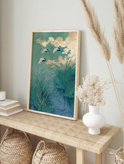 Japanese cranes in flight over water with green reeds and golden clouds, illustrative art, in an alternate framed mockup