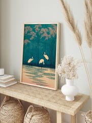 Japanese woodblock style print of three white cranes in teal water with pink foliage and tall, in an alternate framed mockup