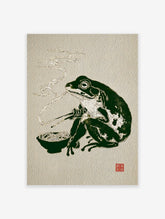 Illustrative Japanese frog art print of a dark green frog eating ramen noodles with chopsticks, with steam rising.