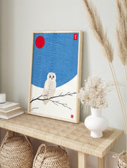 White owl with golden details perched on a branch, red sun and wavy blue sky in Japanese, in an alternate framed mockup