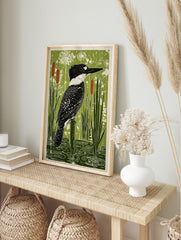 Crested kingfisher bird perched on a post in a green wetland with cattails and water ripples, in an alternate framed mockup