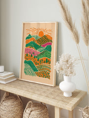Illustrative layered landscape art print with orange sun, green hills, magenta fields, and, in an alternate framed mockup