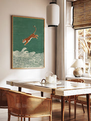Illustrative print of an orange and black tiger leaping over white ocean waves on a textured green, in a styled room mockup
