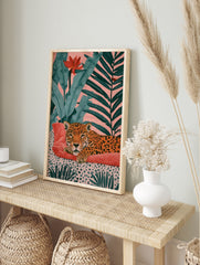 Leopard resting on a red cushion with tropical foliage and a pink background art print, in an alternate framed mockup