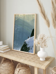 Lone skier in an orange jacket on a steep, snow-covered mountain ridge with layered peaks in, in an alternate framed mockup