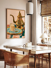 Illustrative art print of a glass of masala chai, a metallic teapot, and cardamom pods on a, in a styled room mockup