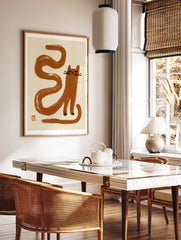Minimalist brown cat illustration with long serpentine tail and red seal mark on cream background, in a styled room mockup