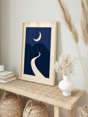 Minimalist night landscape art print with a cream crescent moon over navy blue rolling hills, in an alternate framed mockup