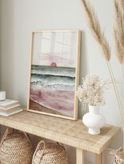 Minimalist watercolour art print of a sunset over the ocean with red sun, green-blue waves, in an alternate framed mockup