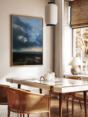 Moody, dark stormy landscape with heavy clouds and a textured horizon line in shades of blue and, in a styled room mockup