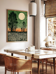 Linocut style moonlit field print with dark green sky, orange horizon, silhouetted trees, and tall, in a styled room mockup