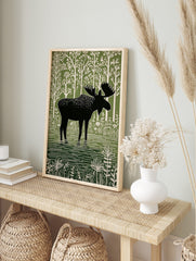 Moose illustration print, black silhouette moose in green water, white stylised trees and, in an alternate framed mockup