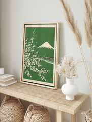 Japanese woodblock style print of Mount Fuji behind white cherry blossom branches on a green, in an alternate framed mockup