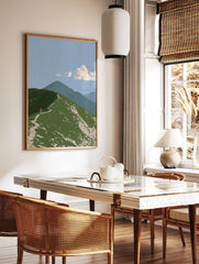 Illustrative mountain ridge wall art with a hiker wearing a red backpack on a green grassy path, in a styled room mockup