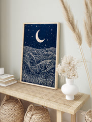 Stylised night ocean illustration with swirling waves, a crescent moon, stars, and grass, in, in an alternate framed mockup