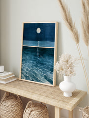 Illustrative wall art of a solitary figure swimming in deep blue ocean water under a full, in an alternate framed mockup