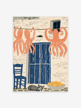 Coral octopuses hanging on a line above a blue door with a striped cat and lemons in a coastal kitchen scene