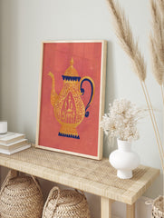Ornate golden teapot with dark blue accents and intricate patterns on a coral background, in an alternate framed mockup