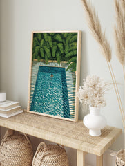 Overhead painting of a person swimming in a turquoise pool with green tropical leaves and, in an alternate framed mockup